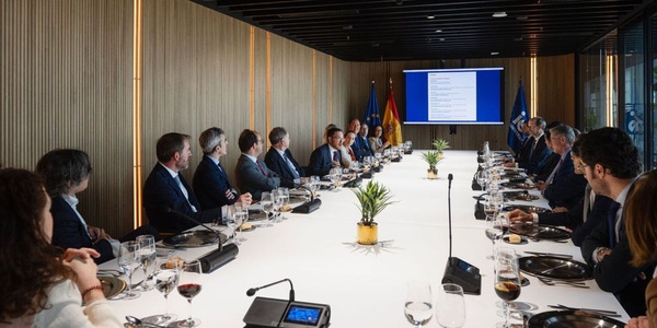 A corporate meeting in a modern conference room with attendees seated at a long table.