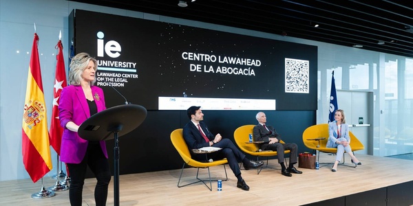 A panel discussion taking place at IE University with speakers seated and one presenter at a podium.