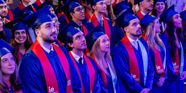 A diverse group of graduates wearing caps and gowns, looking up with anticipation during a ceremony.
