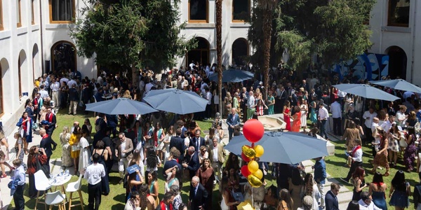 A large outdoor gathering with many people enjoying a sunny day under umbrellas.