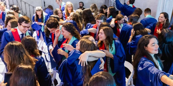A joyful graduation ceremony with students in gowns celebrating and embracing each other.