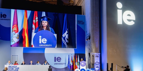 A graduation ceremony at IE University with a student speaking on stage.