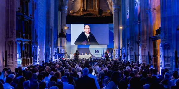 A large audience attending a presentation in a grand hall illuminated in blue light.