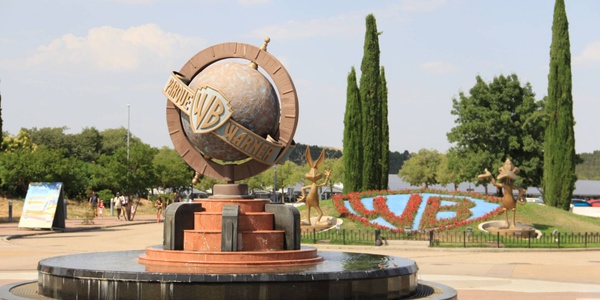 A globe monument with the WB logo surrounded by greenery and decorative elements.