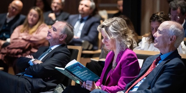 A group of people attending a presentation, with a woman reading a book in the foreground.