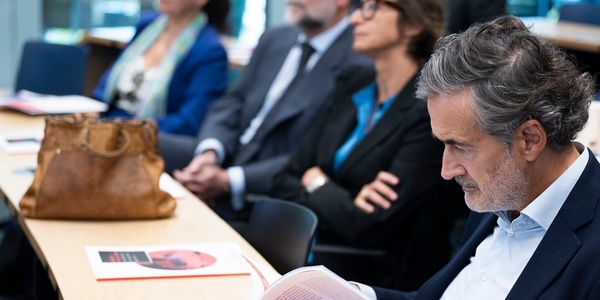 A group of professionals attending a conference, with a focus on a man reading a document.