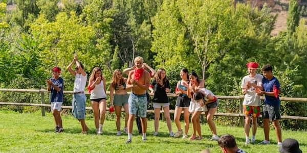 A group of people of various ages engaging in a playful activity outdoors in a grassy area with trees in the background.