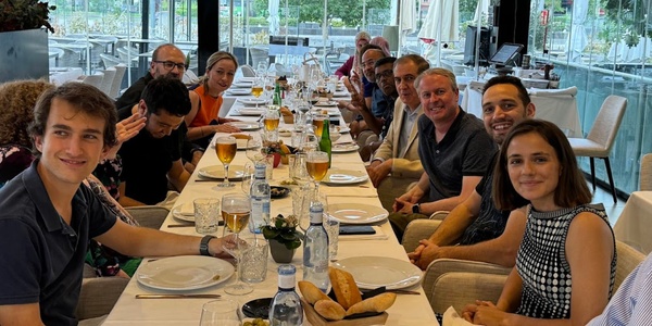 A group of people sitting at a long dining table in a restaurant, smiling at the camera.