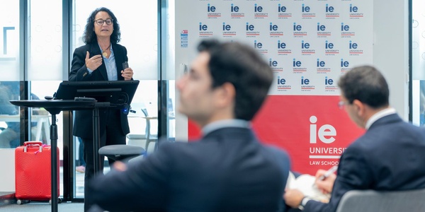 A speaker presents at a law school event with attentive audience members in the background.