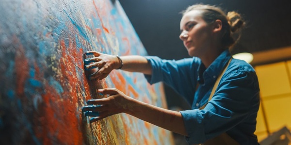A woman is painting on a large canvas using her hands with colorful paint.