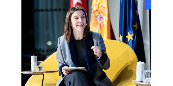 A woman in a gray blazer sits comfortably while engaging in discussion.