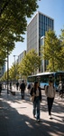 A bustling urban street lined with modern buildings and trees, featuring pedestrians and a bus.