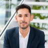 A professional man in a suit sitting with a modern office background.
