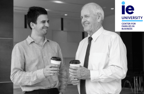 Two men, one younger and one older, smiling and holding coffee cups in an office setting