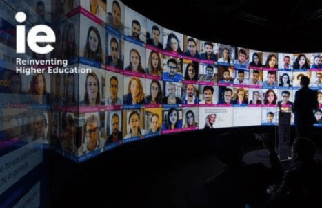 People observing a large digital display featuring a collage of diverse individual portraits at an event themed 'Reinventing Higher Education'.