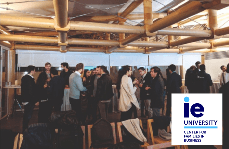 A group of people networking at an indoor event, with some visuals of IE University's logo and the Center for Families in Business.