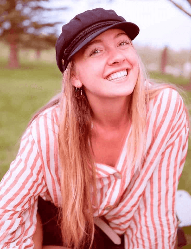 A smiling woman wearing a black cap and a striped shirt sitting outdoors.