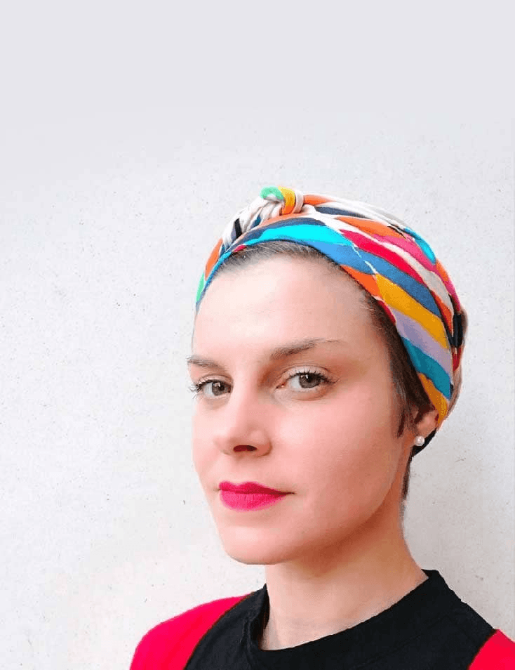 A woman with a colorful headscarf and red lipstick poses against a plain background.