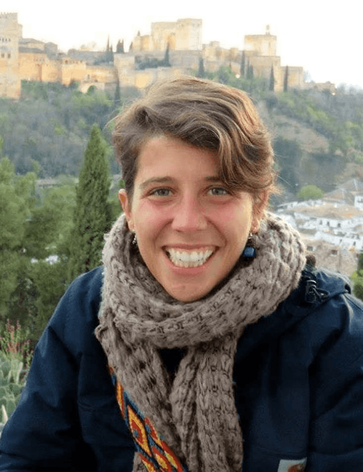 A smiling woman with short hair wearing a scarf, with the Alhambra in the background.