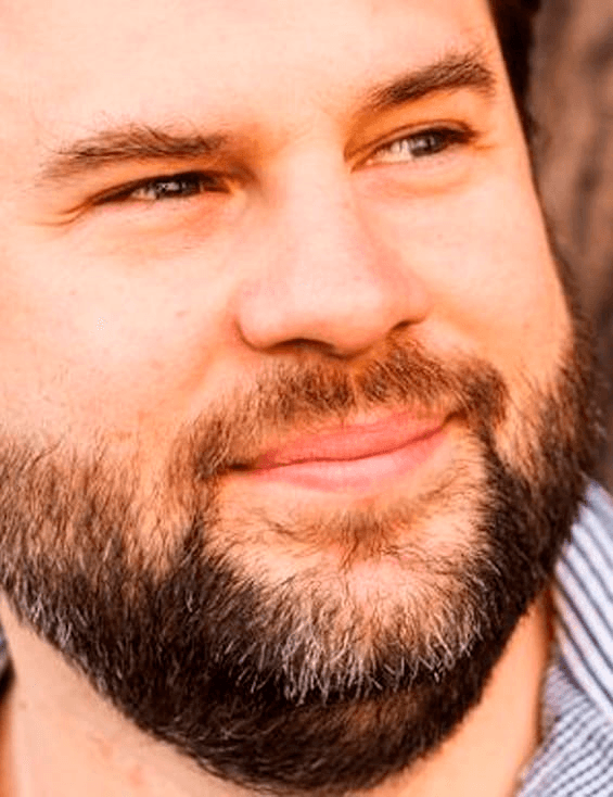 Close-up portrait of a smiling man with a beard and a checked shirt.