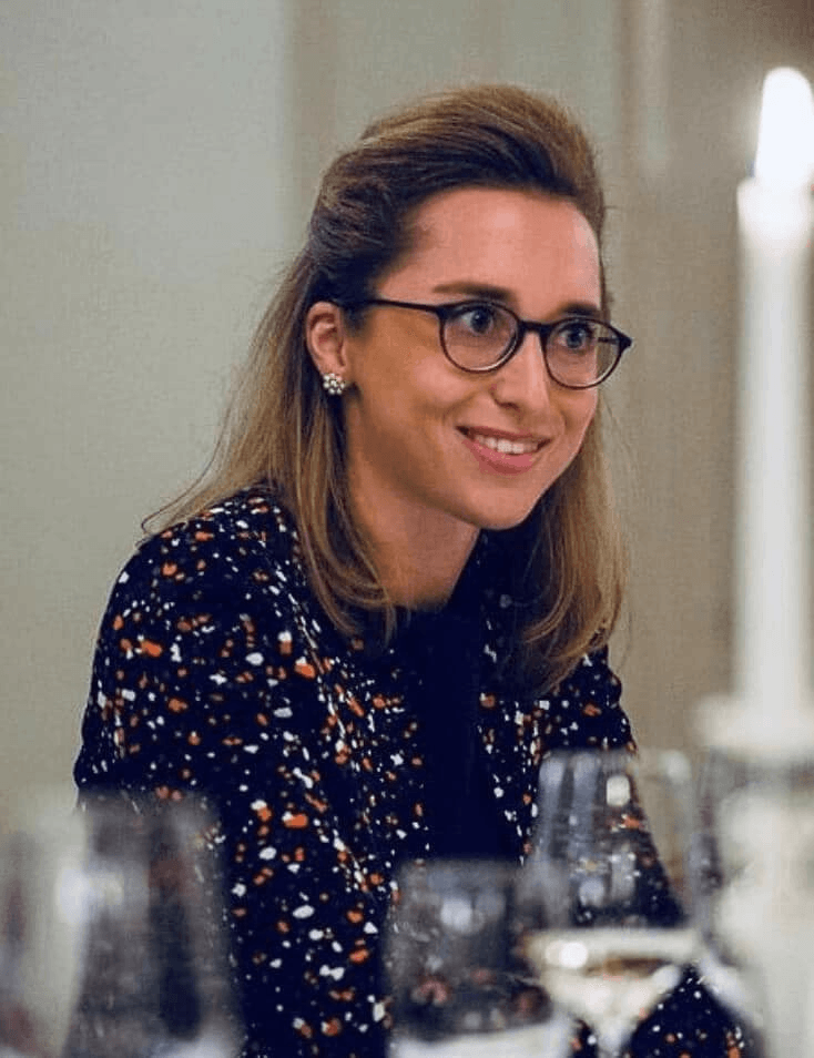 A smiling woman with glasses wearing a patterned dress at a dinner setting.