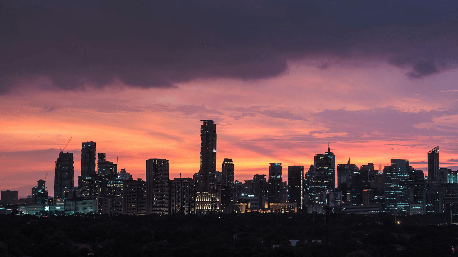 A city skyline silhouetted against a vibrant sunset.