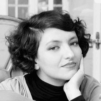 Black and white photo of a woman with short curly hair, resting her chin on her hand and looking thoughtfully at the camera.