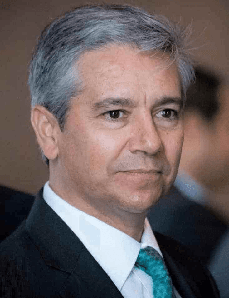 A mature man with gray hair wearing a suit and a turquoise tie