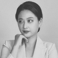 A black and white portrait of a young woman with a contemplative expression, wearing a light-colored blazer and resting her chin on her hand.