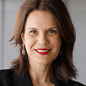 A professional portrait of a woman with short dark hair, smiling, wearing a black blazer and red lipstick.