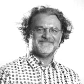 Black and white portrait of a smiling middle-aged man with curly hair and glasses, wearing a patterned shirt.