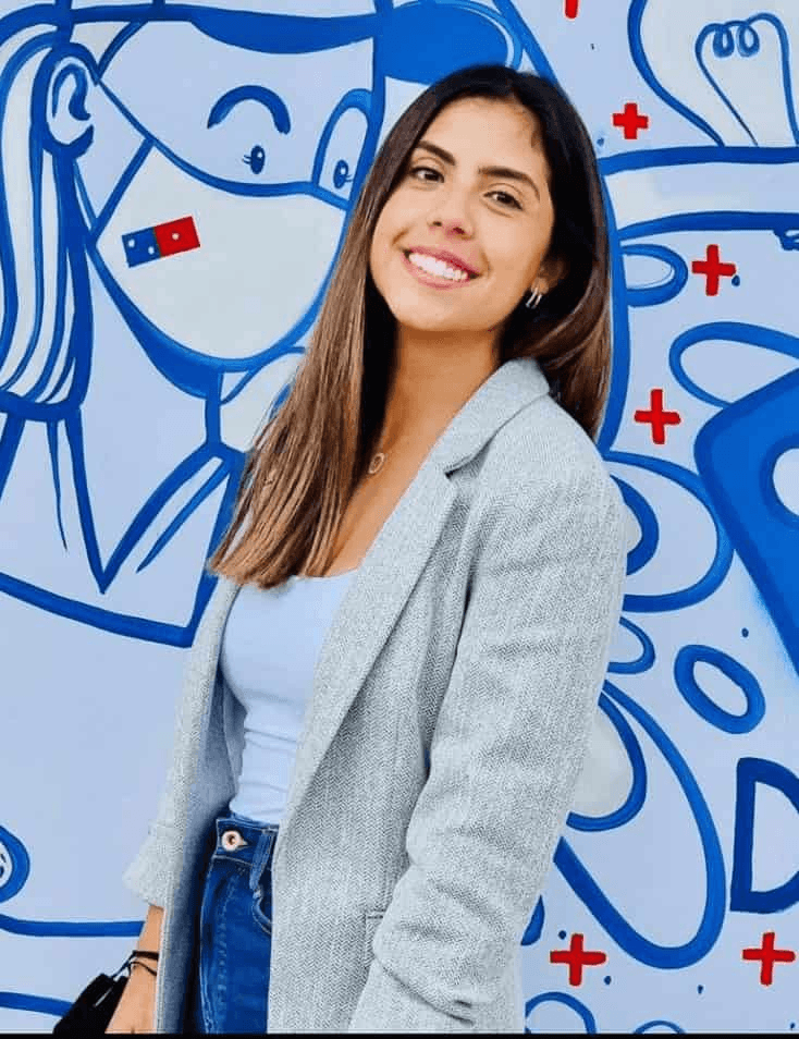 A smiling young woman standing in front of a colorful mural with cartoon-style artwork.