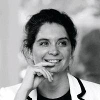 A black and white portrait of a smiling woman with her hand on her chin, looking thoughtful.