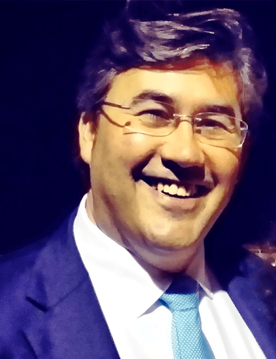 A smiling man wearing glasses, a blue suit, and a blue tie.