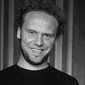 Black and white photo of a smiling man with curly hair.
