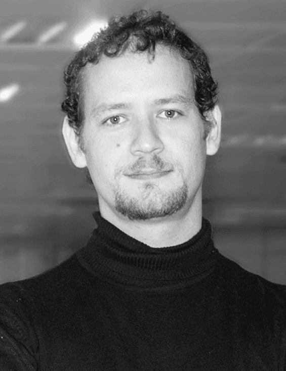 A black and white photo of a smiling man with curly hair wearing a turtleneck sweater.