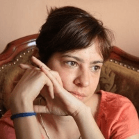 A woman with short brown hair resting her chin on her hands, looking thoughtful.