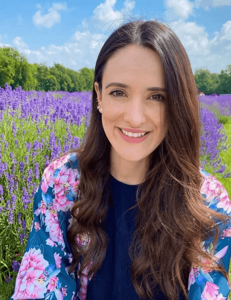 A woman smiling in a field of purple lavender under a clear blue sky.