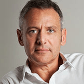 A portrait of a middle-aged man with short gray hair, wearing a white shirt, looking directly at the camera with a serious expression.