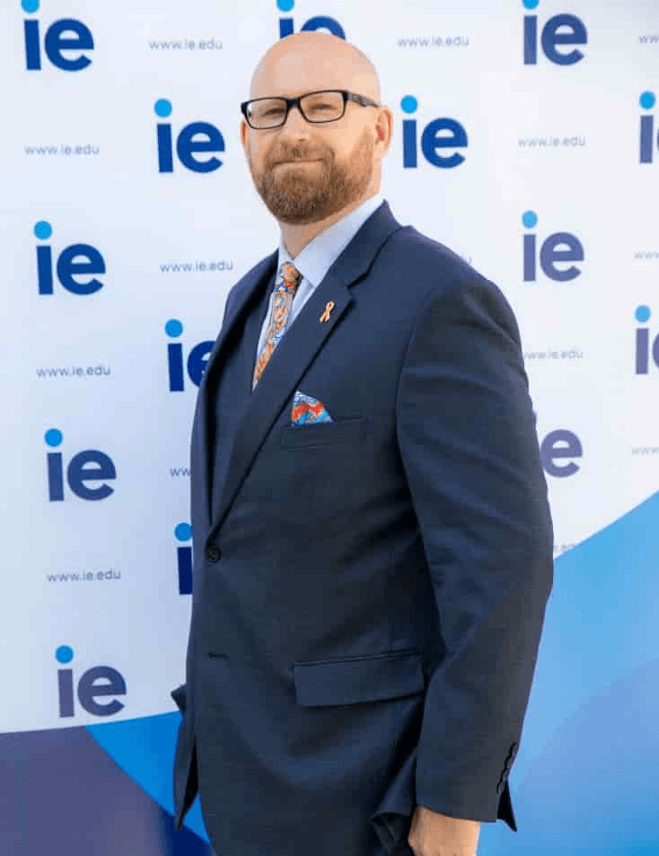 A man in a suit stands in front of a backdrop displaying the 'ie.edu' logo.