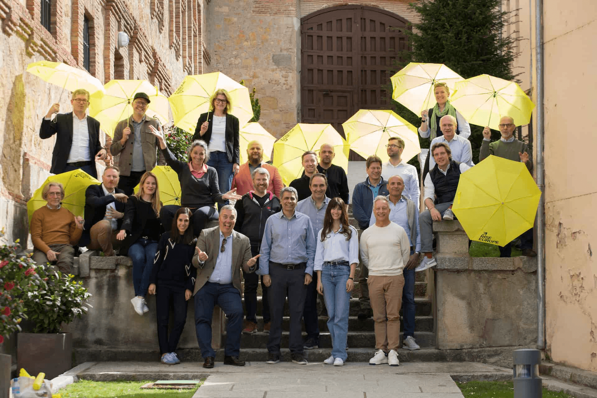 A group of people holding yellow umbrellas posing on steps outdoors.