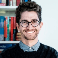 A smiling man with glasses standing in front of a bookshelf.