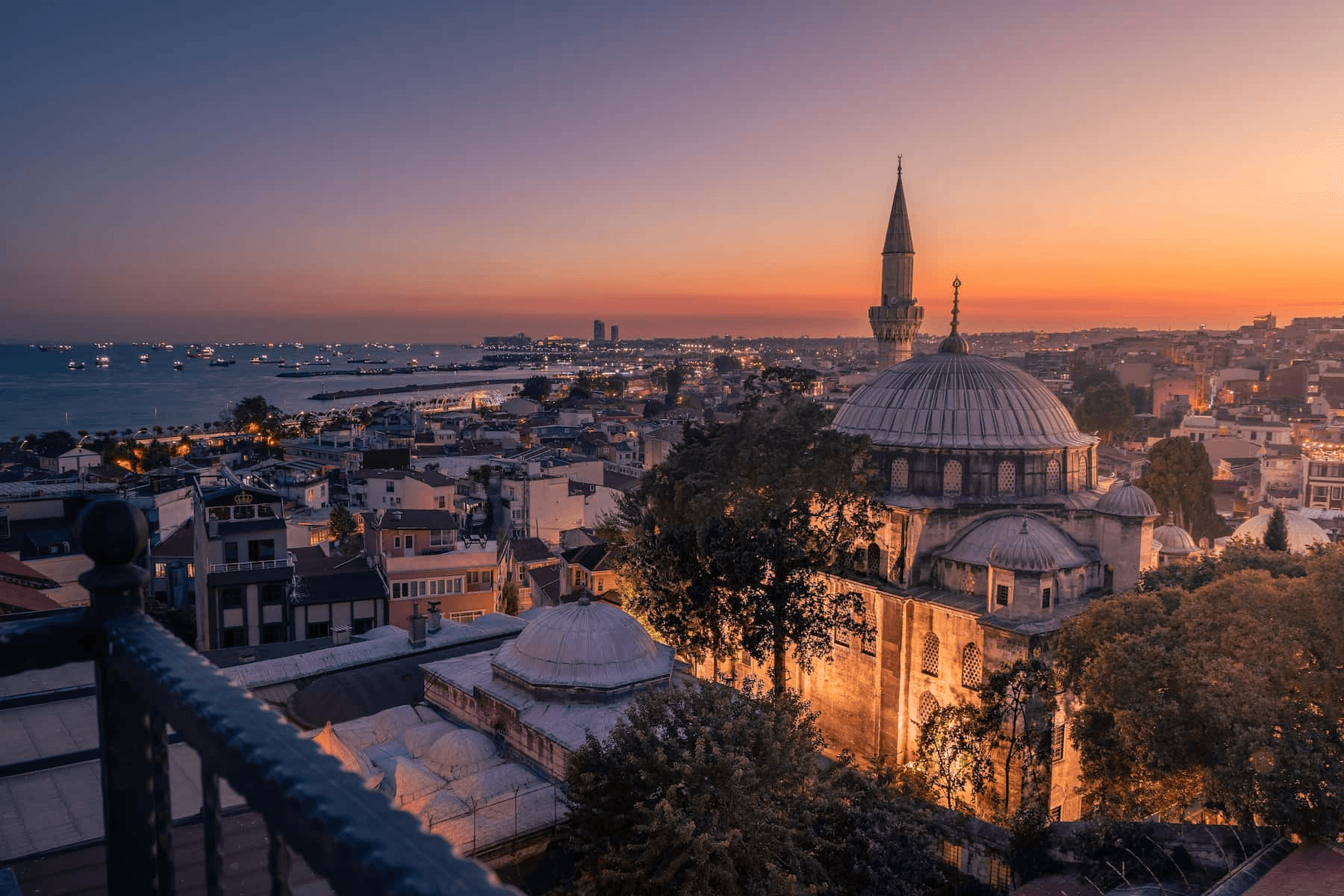 Sunset view over a historic cityscape with a mosque and the sea in the background.