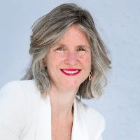Portrait of a smiling middle-aged woman with grey hair wearing a white blazer against a white background.