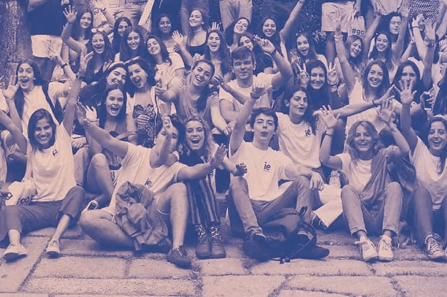 A large group of smiling young people sitting on steps, waving their hands.
