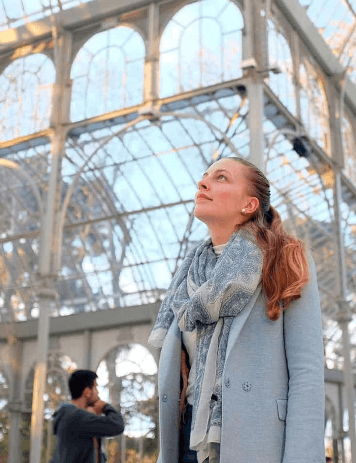 A woman admiring the architecture of a large glass structure, with a man in the background.
