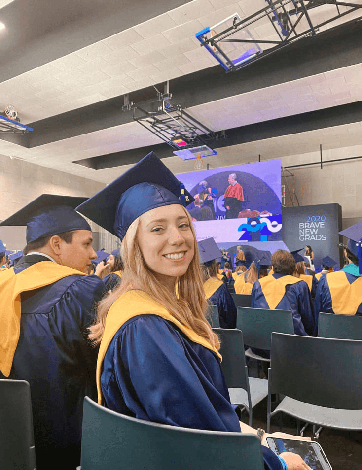A young woman in a graduation cap and gown smiles at a graduation ceremony.