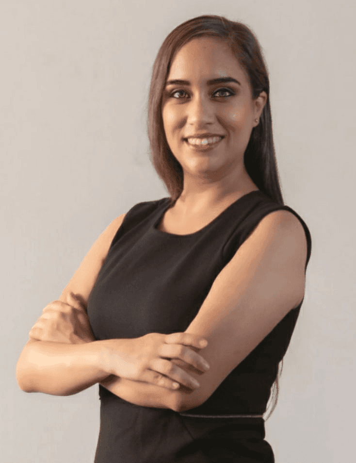 A confident young woman in a black sleeveless dress, smiling and standing with her arms crossed.