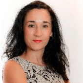 A professional portrait of a woman with dark, curly hair and a patterned dress.