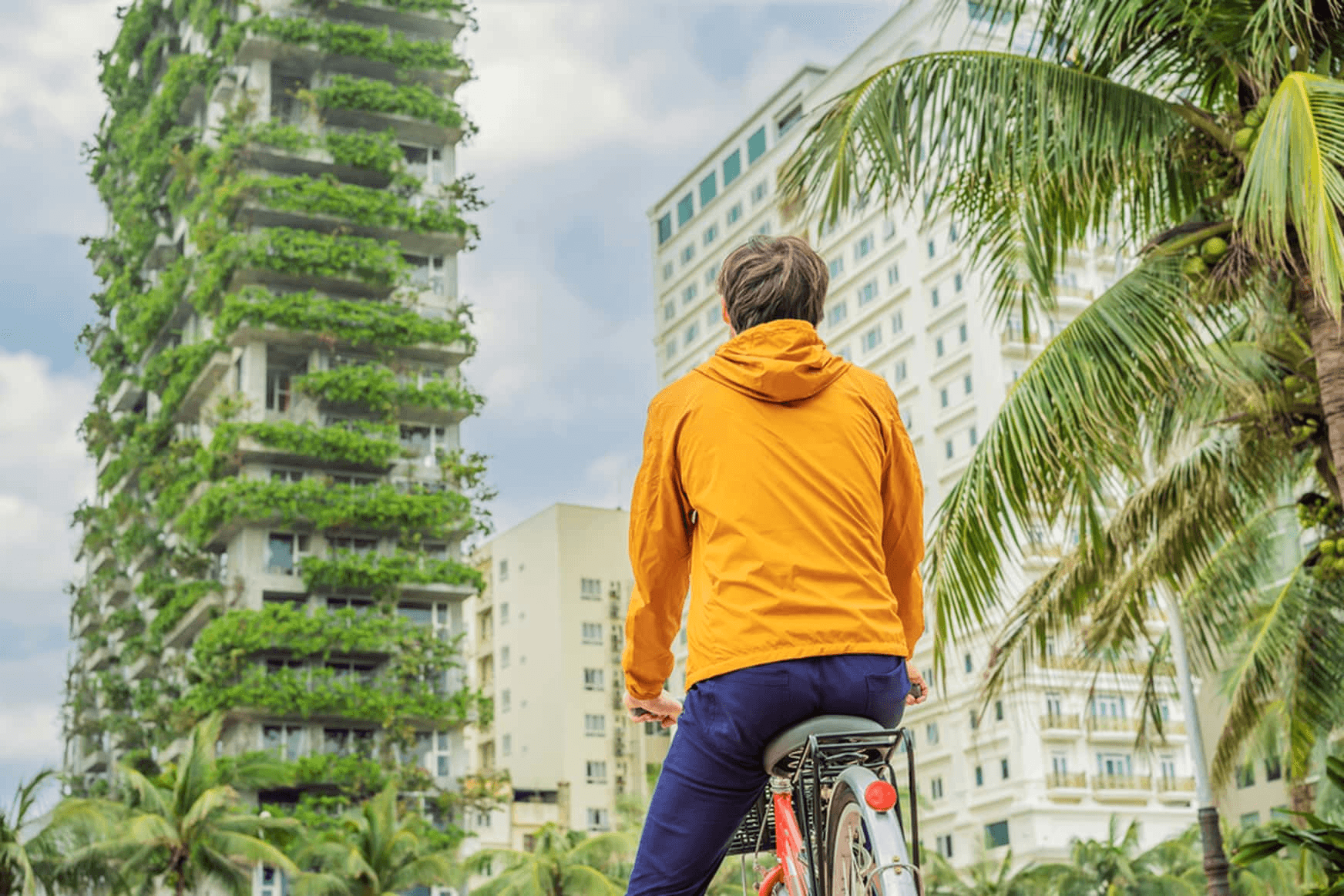 IE student on a bike with a yellow jacket looks at a nature fully covered building